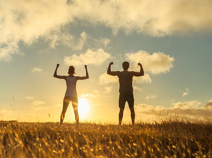Multivitamins - A woman and a man showing off their biceps looking at the sun.